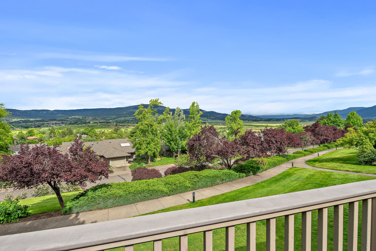 Photo of the view from a balcony at a Rogue Valley Manor cottage, with trees, rolling hills and a few other residences.