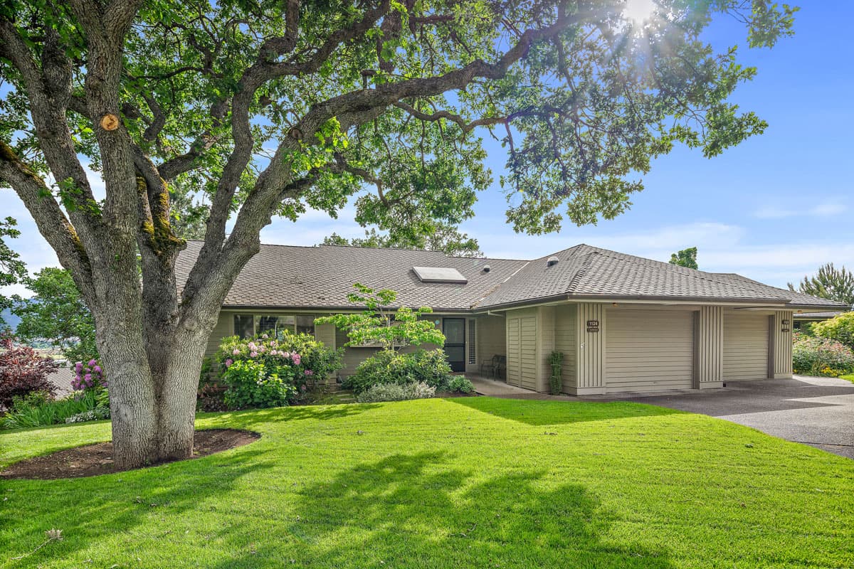 Exterior view of a Rogue Valley Manor cottage with green grass and a large tree out front.